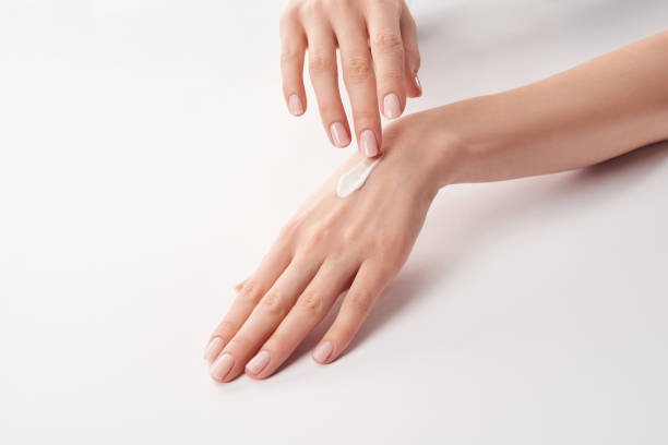 Partial view of woman applying cosmetic cream on white background